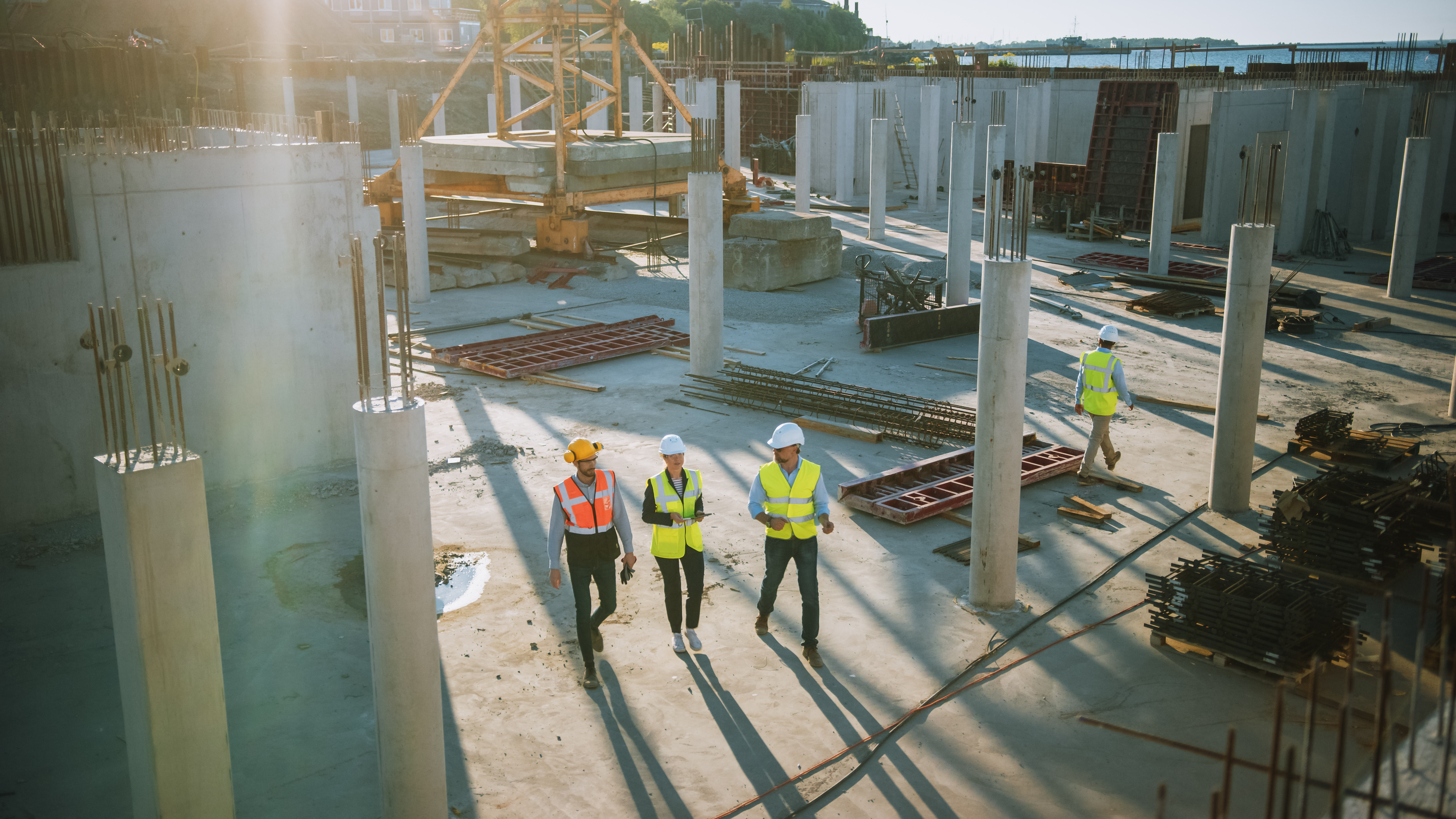 Construction site with Kiwa auditors in safety gear inspecting concrete columns under sunlight.