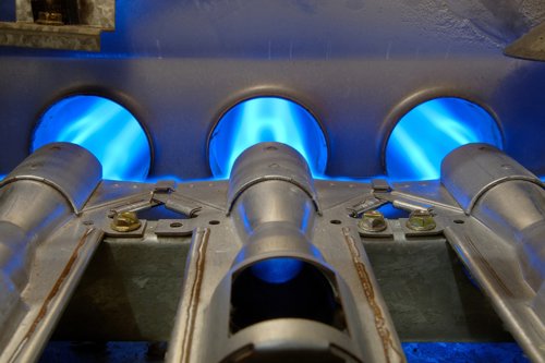Close-up of a gas furnace with three blue flames burning inside metal tubes.