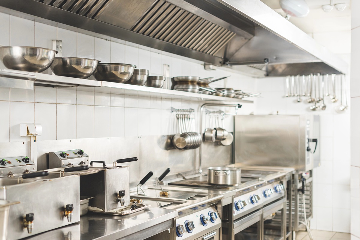 Professionele keuken met roestvrijstalen apparatuur, kookplaten, ovens, pannen en wandrekken met keukengerei.