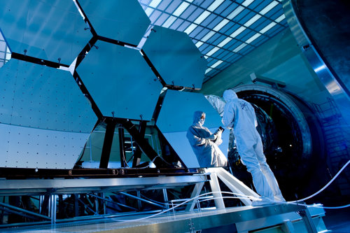Scientists in clean suits working on large hexagonal mirrors in a laboratory, highlighting advanced technology and precision engineering