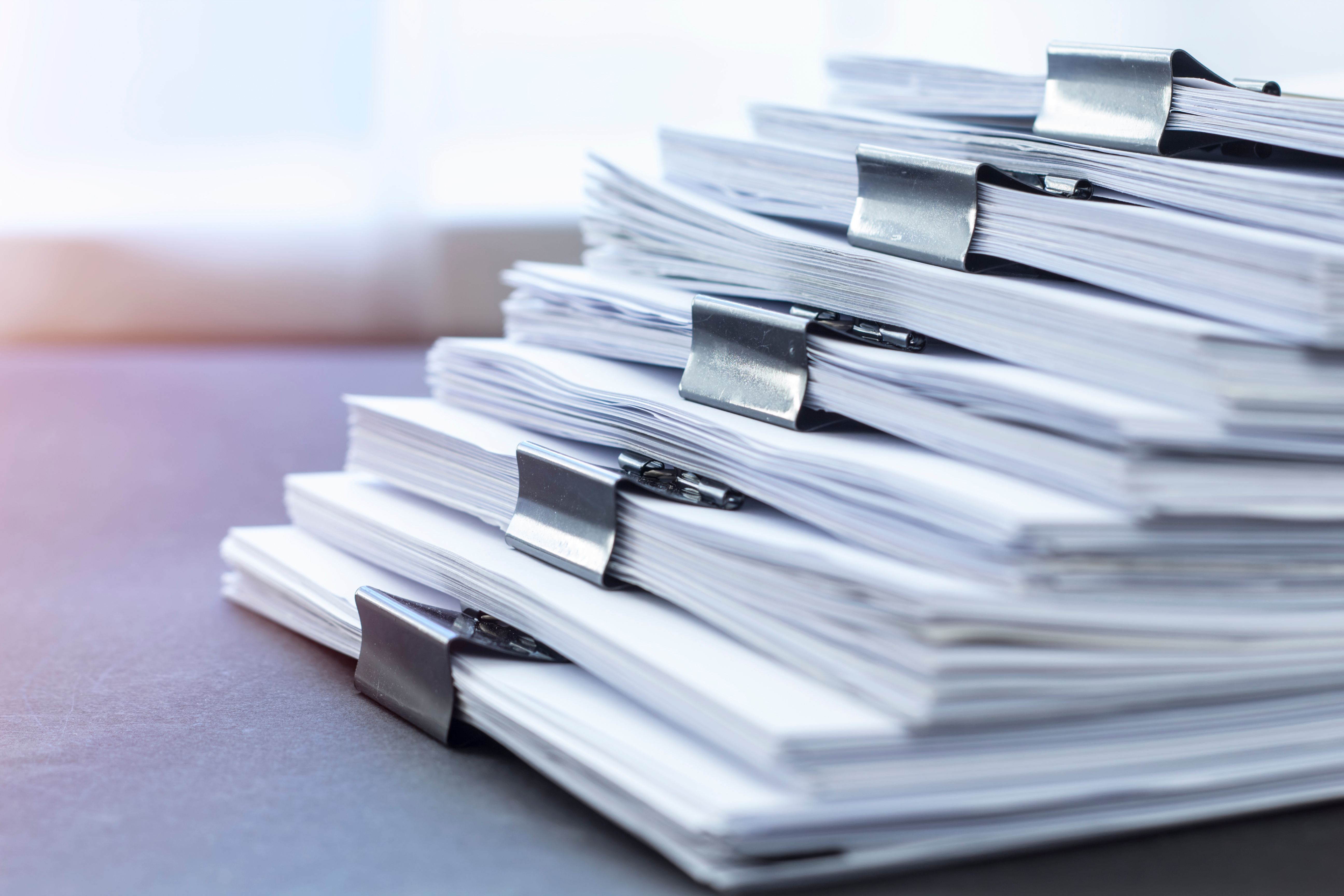 Stack of clipped paper documents on a desk, office paperwork in neat piles