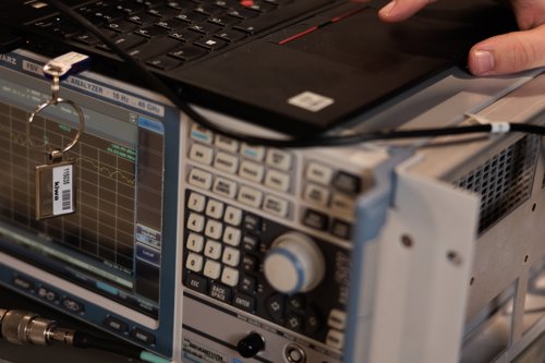 A hand operating a laptop connected to an electronic signal analyzer in a laboratory setting