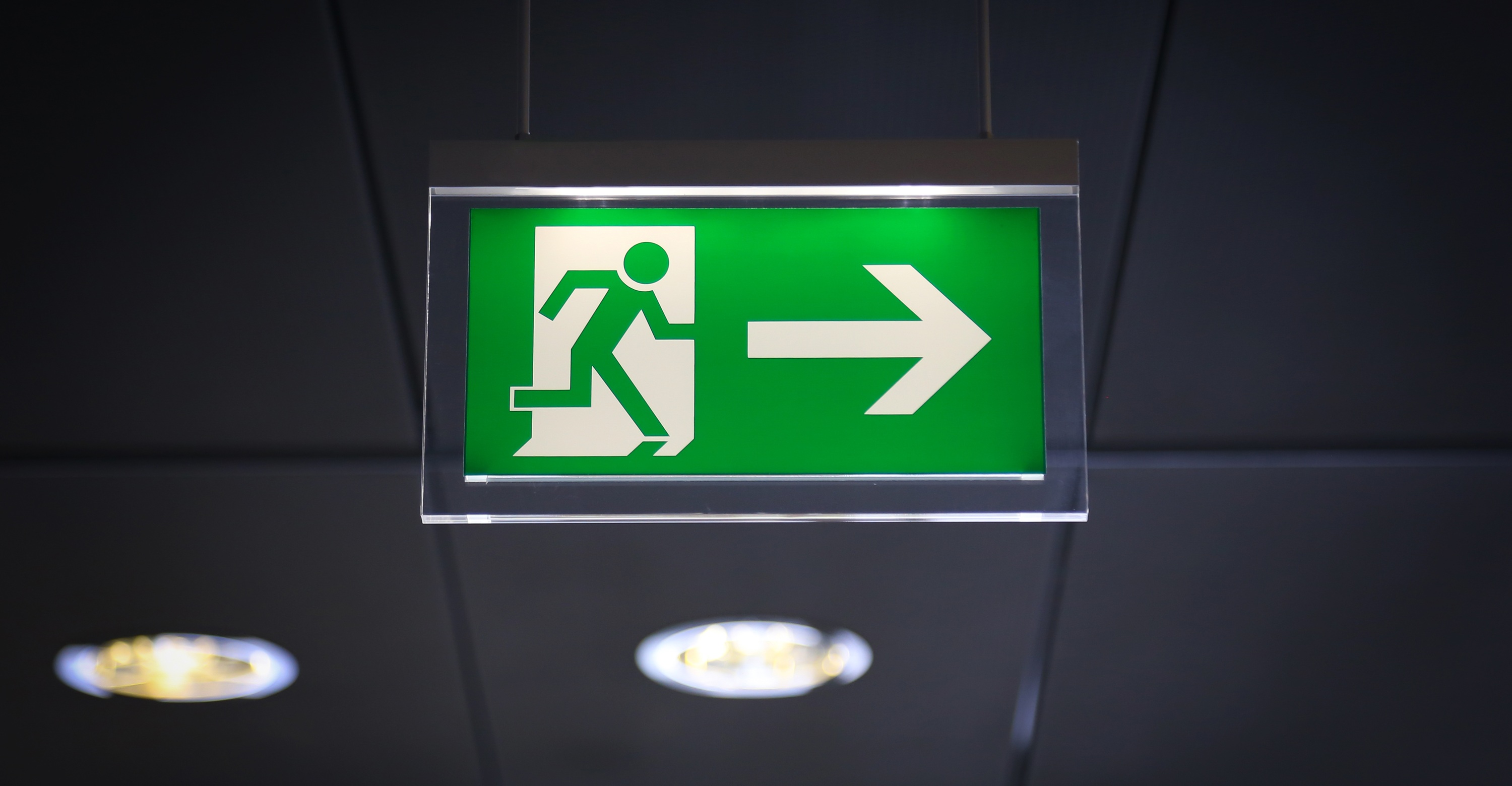 Groen nooduitgangbord, hangend aan een plafond.