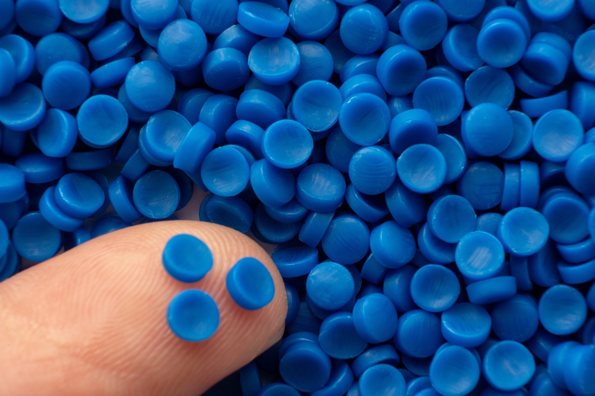 Close-up of a fingertip touching a pile of small blue plastic pellets.