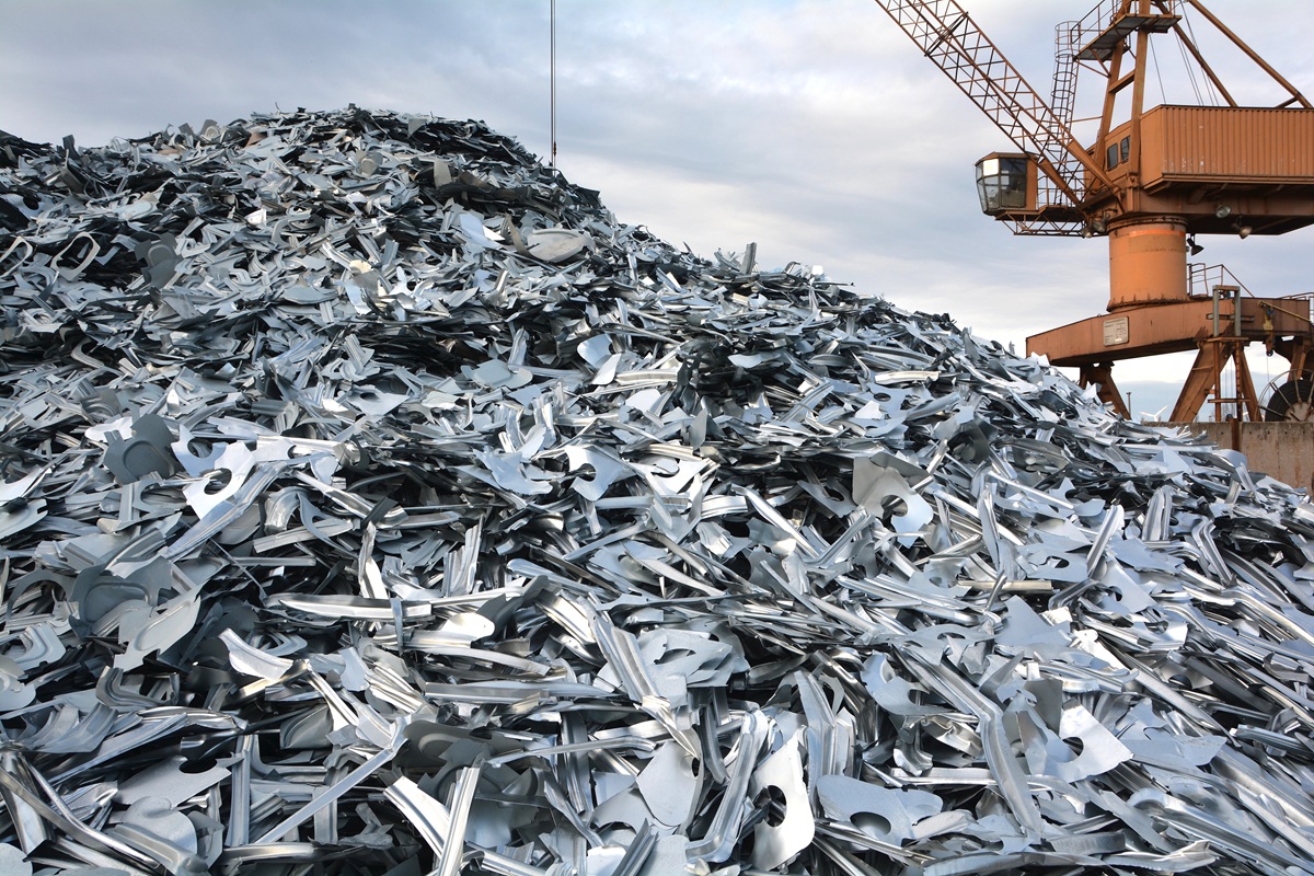 Large pile of shredded metal scrap at an industrial recycling yard with a crane in the background.