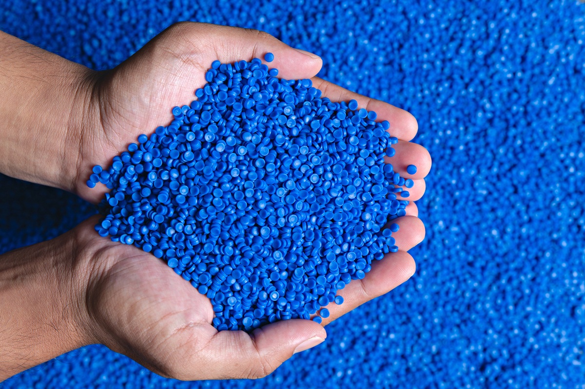 Hands holding a heap of blue plastic pellets on a background of blue granules.