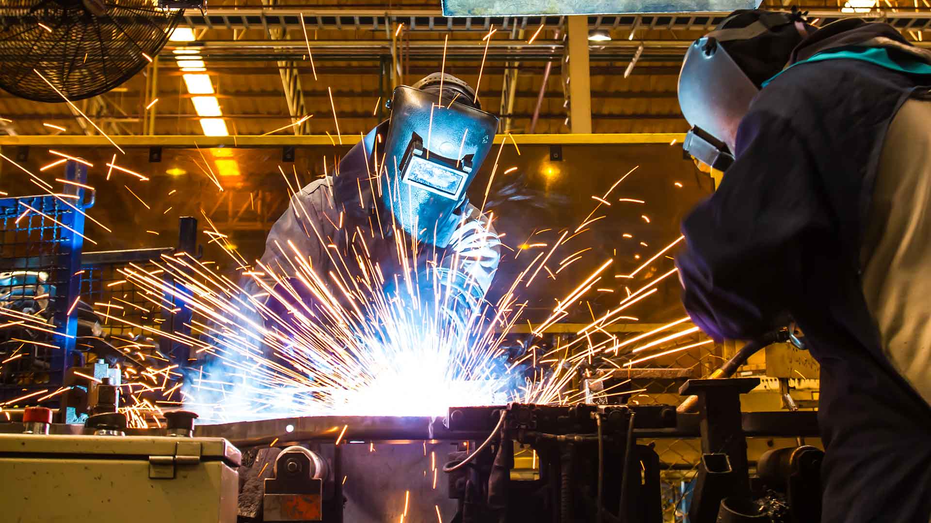 Två svetsare med svetshjälm arbetar i en industrimiljö med kraftiga gnistor under svetsning - med hjälp av Kiwas tjänst för svetsvalidering enligt IEC 60974-14 får du både validering och kalibrering av din svetsutrustning.