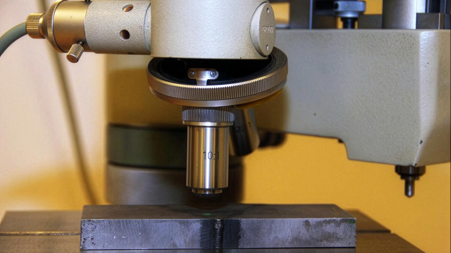 Närbild av ett mikroskop som används för att undersöka en mörk metallisk yta enligt Makroskopisk undersökningsmetod inom förstörande provning.