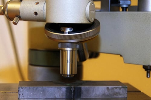 Närbild av ett mikroskop som används för att undersöka en mörk metallisk yta enligt Makroskopisk undersökningsmetod inom förstörande provning.