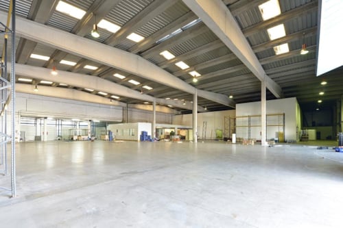 Ett stort tomt industrilager med betonggolv och takfönster i taken och betongbalkar som stödjer dem.