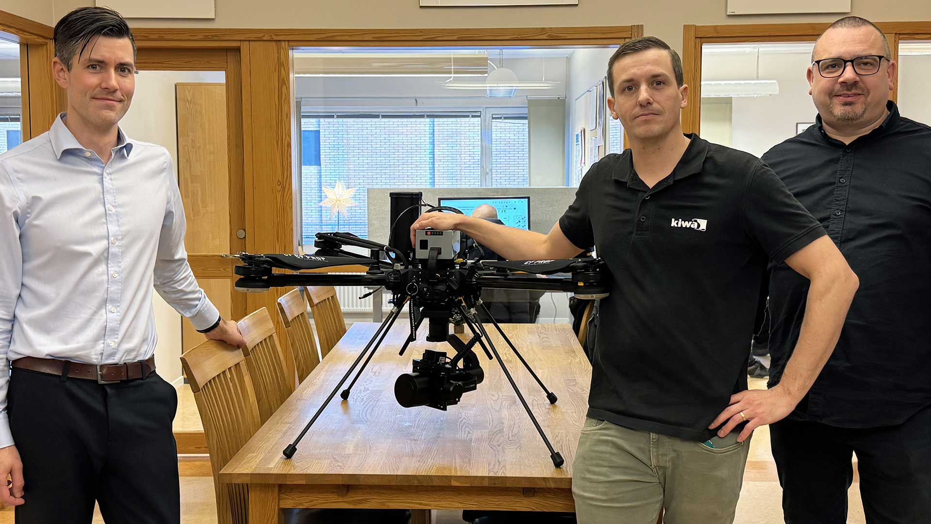 Tre personer från Kiwa står runt Tundra-drönaren på ett mötesbord i ett kontor.