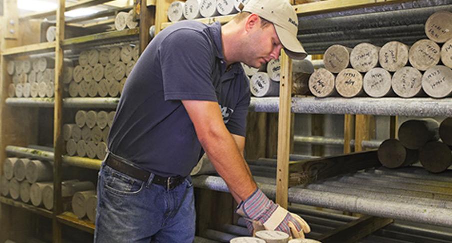 Kiwa engineer wearing a cap and gloves handling soil samples on industrial storage racks in a warehouse.