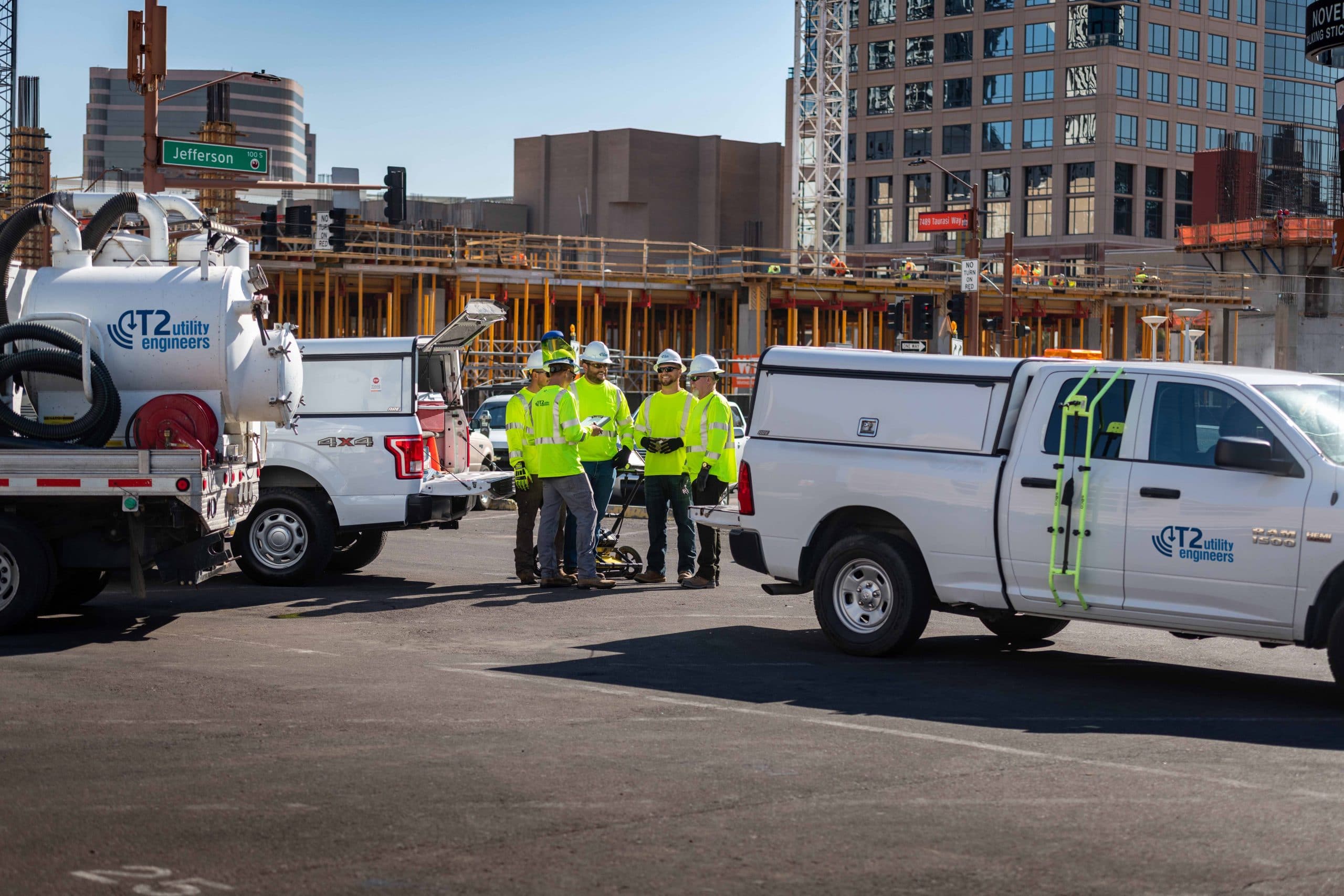 Utility engineers in neon safety gear standing beside white work trucks at a city construction site.
