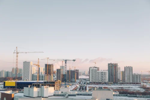 Urban skyline with high-rise apartment buildings under construction and multiple cranes at sunrise.