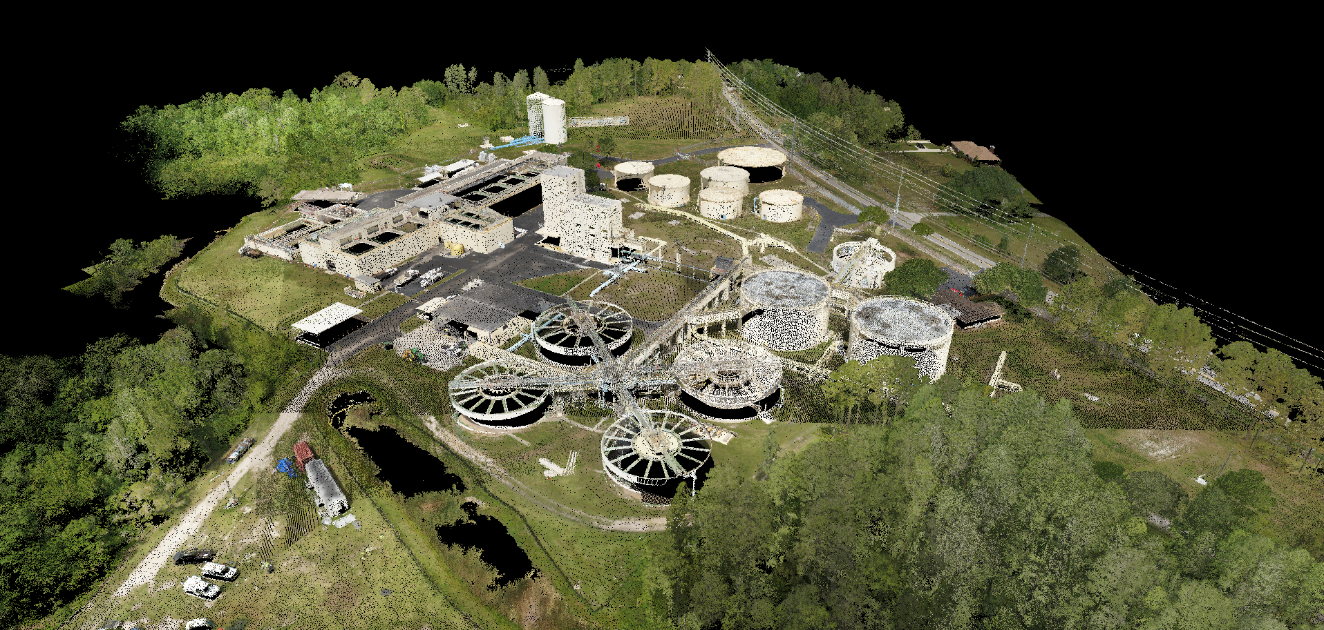 Aerial view of an industrial wastewater treatment plant with circular clarifiers, tanks, buildings, roads, and surrounding trees.