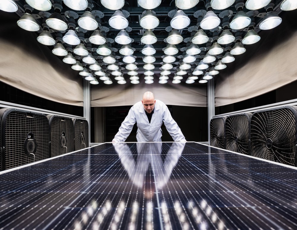 Kiwa PVEL employee in a laboratory conducting solar panel efficiency tests under artificial lighting conditions, surrounded by fans.